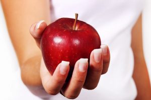 Fastenzeit: Das Bild zeigt einen weiblichen Arm und eine Hand, die einen roten Apfel hält.