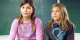 Liebe: Das Bild zeigt zwei Mädchen im Alter zwischen 9 und 11 Jahren. Sie sitzen in einem Klassenraum auf dem Pult und erzählen.